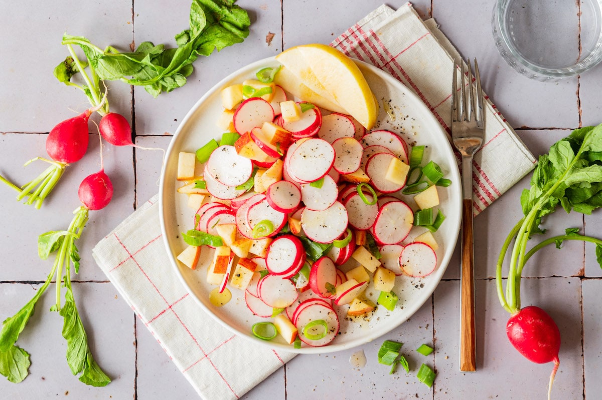 Radish apple salad with scallions on a white plate.